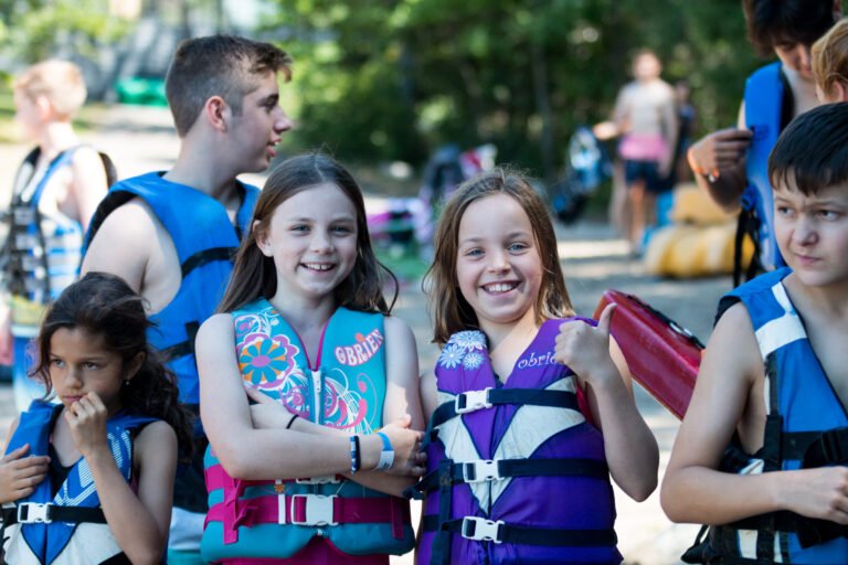 Two children wearing life vests smile at the camera.