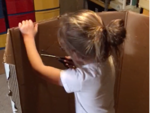 a young girl cuts a hole in cardboard