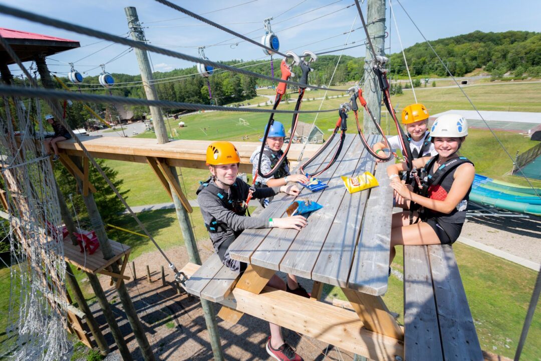 Four young people sitting at a picnic table on a ropes course