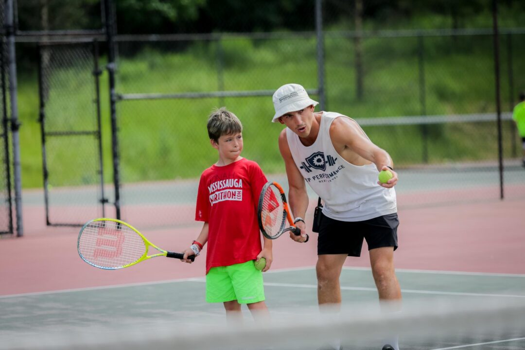 a young boy learns to play tennis from an instructor