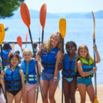 Muskoka Woods summer camp guests wearing lifejackets and holding paddles on the beach